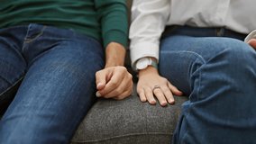 A man and woman in casual attire sitting closely on a sofa, holding hands, symbolizing love and companionship in a cozy home setting. - Powered by Shutterstock - Get 15% off with code: PIKWIZARD15