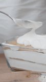 The woman is preparing tiramisu, she spreads the top layer of cream evenly. Vertical video.