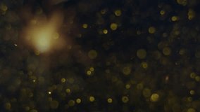 Particles of gold color fall on a dark  background in an abstract order, beautiful reflection of glare from the light, bokeh and out of focus glare. Slow motion, 8K downscale, 4K.