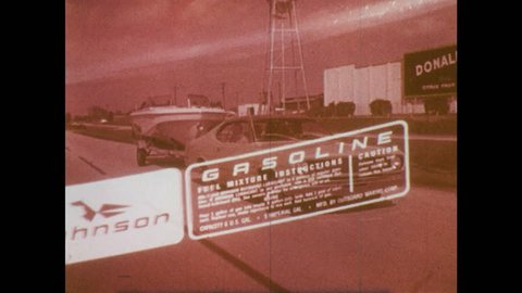 1970s: Red gasoline transfer tank being fueled as gas pump, man screws lid on. Man launches boat from trailer, boy with rope prevents boat from drifting off.