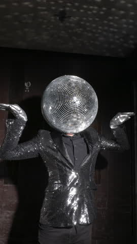 A man with a sparkling discoball suit dancing in an industrial elevator in vertical