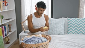A smiling latino man in a tank top enjoys music on red headphones while folding laundry in his well-lit bedroom. - Powered by Shutterstock - Get 15% off with code: PIKWIZARD15