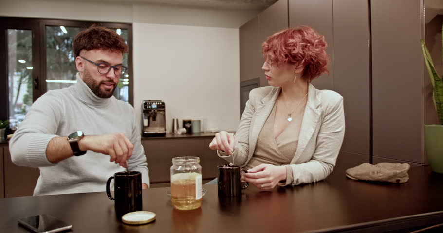 A young man and woman casually converse over coffee in a modern office kitchen, enjoying a relaxed break together, fostering a friendly work environment.