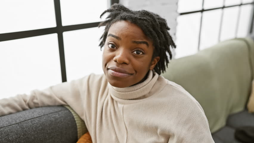 Cheerful young black woman with dreadlocks sitting comfortably on sofa indoors. with a smile and a point to her head, she reveals a great idea. a happy memory from home. Royalty-Free Stock Footage #3468048277