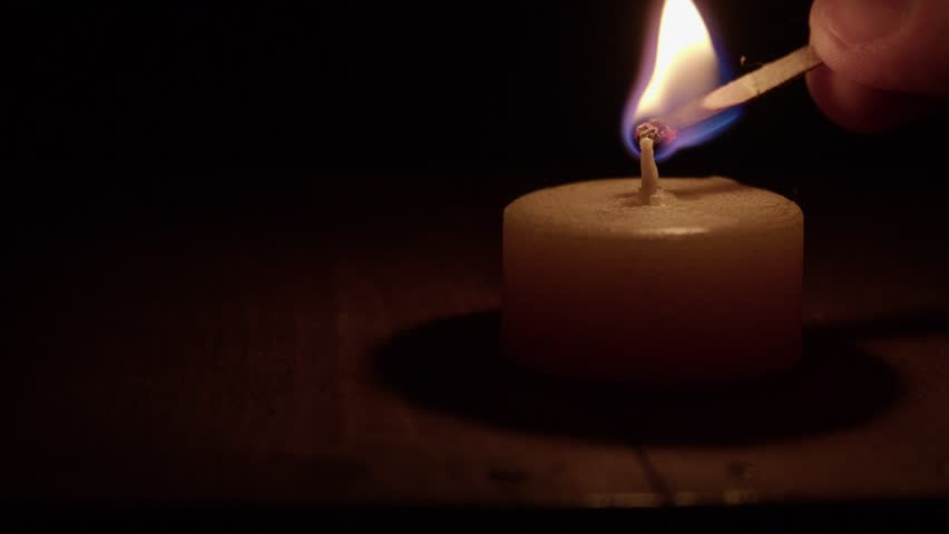 Closeup: Golden bees wax candle it lit with match in dark black room