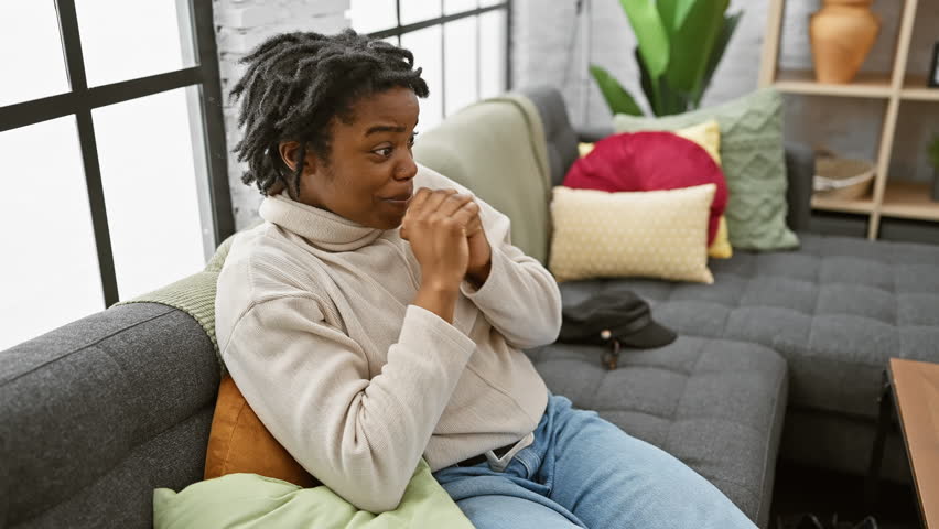 Joyful young black woman with dreadlocks celebrating a big win at home, screaming with excitement while sitting on the sofa, portrait of success with winner gesture!