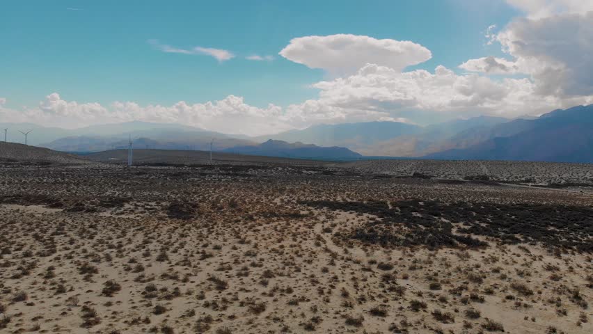 Slow fly over pulling back of sand and brush covered hills near small desert town