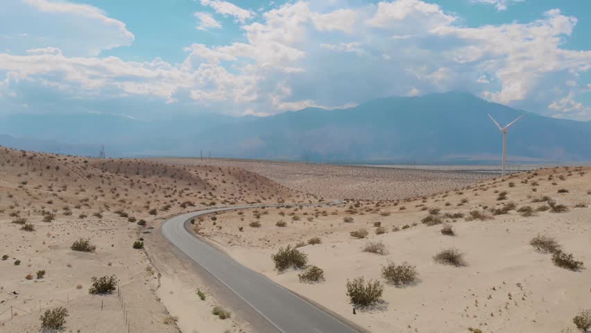 Drone side scroll of sand and brush covered hills near small desert town and windmill