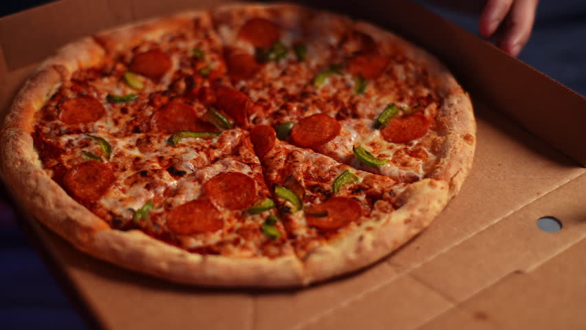 Detail cropped shot of unrecognizable man taking piece slice of hot delivery tasty pizza from cardboard box at home. Closeup of male hands taking pizza slices in dark room. Shooting in slow motion.