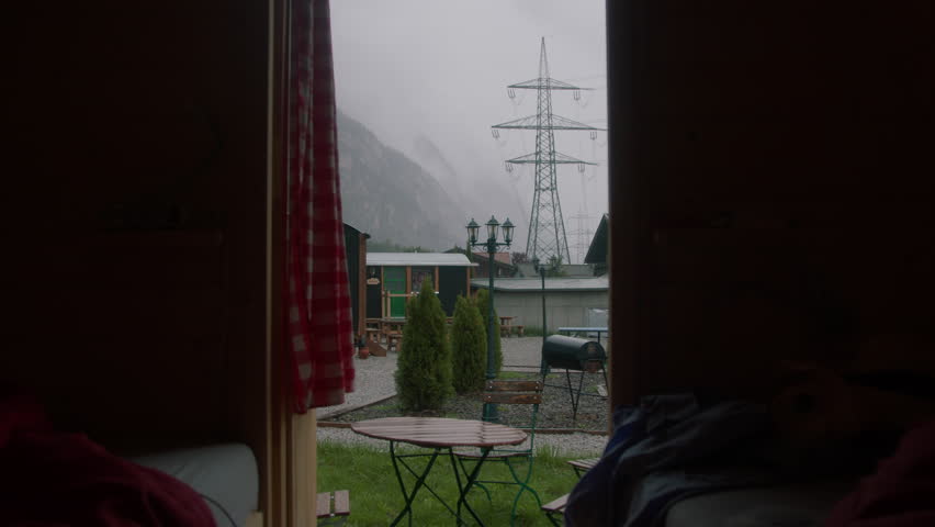 View from inside the house, a small outdoor seating area with a round table and chair, barbecue, with a high voltage tower and fog-covered mountains in the background