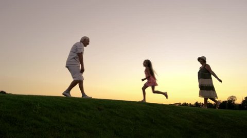 Smiling granddaughter running to grandfather outdoors. Happy meeting of little girl with grandfather at sunset sky. People spending happy time together outdoors.
