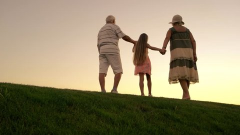 People walking on evening sky background. Girl and grandparents holding hands and walking beyond horizon. Leave the past behind.