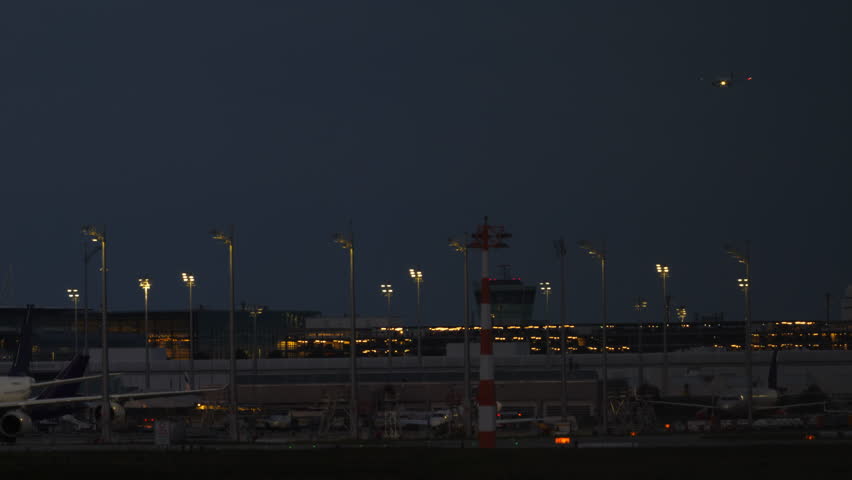 Airplane with landing lights on approaching an airport terminal at night, with runway and terminal lights illuminated in the background