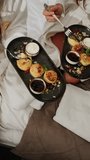 Two young women in bathrobes are having breakfast in bed. Healthy breakfast cheesecakes. Hotel holiday concept. Vertical video