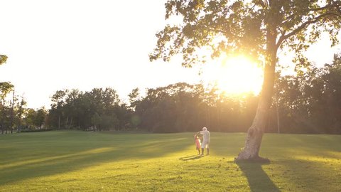 Grandfather spinning granddaughter in park. Elderly man and grandchild having fun on nature background, sunny day. Enjoying time together.