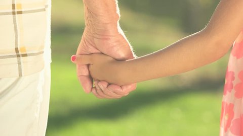 Hands of girl and grandfather together. Granddaughter holding hand with her grandfather on summer nature background. Support and protection.