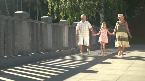 Happy family walking together. Lovely cheerful girl holding hands with grandparents and walking outdoors. Happy weekend with family.