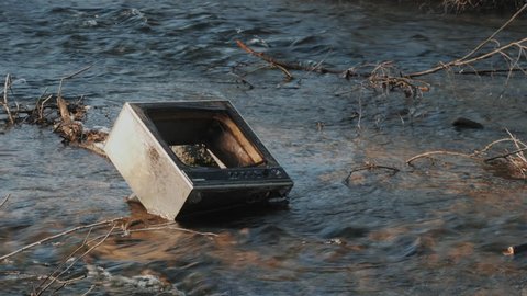 Old retro TV in the river after the flood. The debris from the houses. Pollution of the environment, ecology.