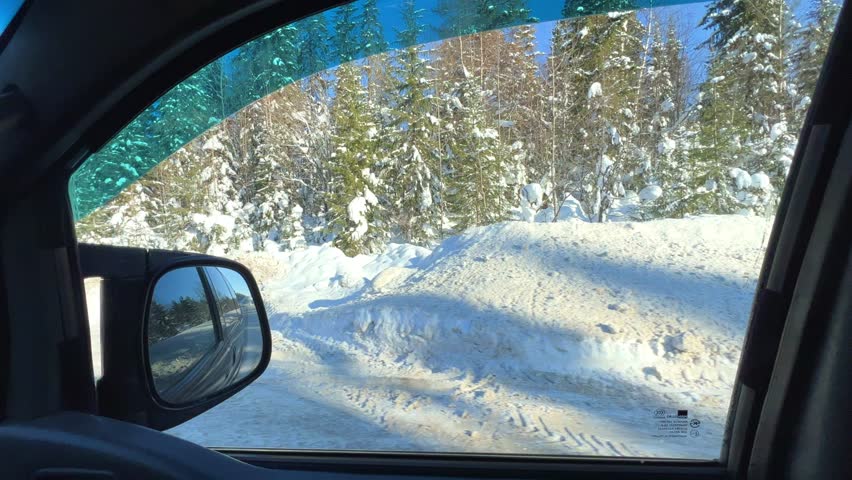 A trip along the winter road past the fir forest. View of the snow-covered trees from the window of a moving car. The reflection of the winter forest in the side view mirror. Trees covered with snow. 