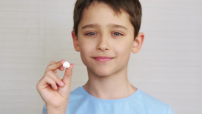 A happy boy holding a vitamin pill. Child in background, close-up vitamin pill in child's hand. Vitamins, children's health, pharmacy business