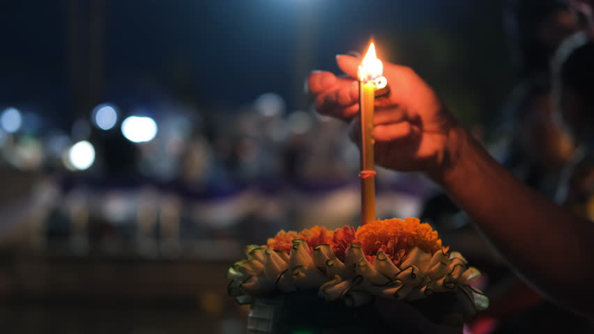 Close-up of hand of unrecognizible man lighting candle in Loy Krathong while praying to water goddess, selective focus