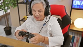 Senior woman happily gaming in a modern room with headset and controller, expressing joy and surprise.