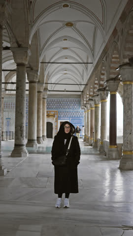 Smiling woman with glasses and headscarf standing in ancient ottoman architecture in istanbul.