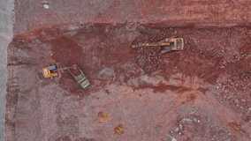 A yellow excavator digs the ground while working in a quarry. Dump truck in a quarry. A truck throws stones from its bed while working in a pit. Aerial photography from a drone. accelerated video.