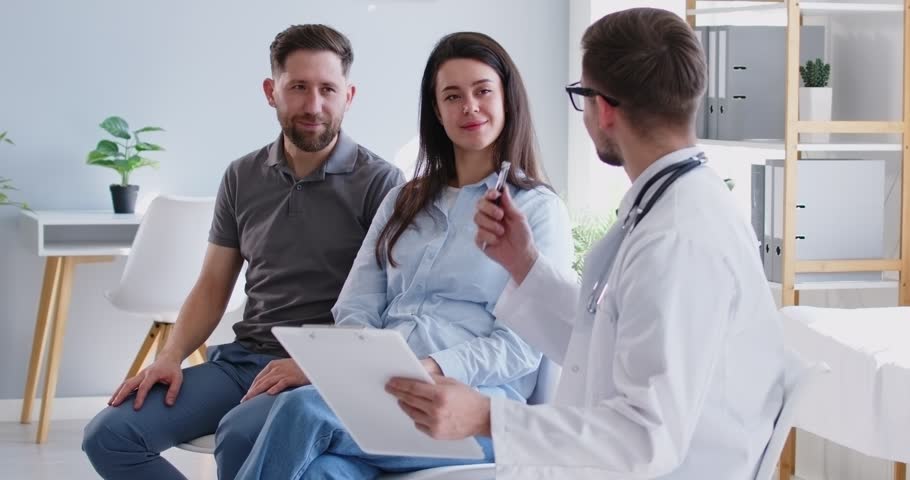 Gynecologist is consulting a family couple, planning pregnancy or IVF during a hospital visit. Couple is happy and engaged in a medical session with the doctor, seeking guidance to future parenthood. Royalty-Free Stock Footage #3468737885