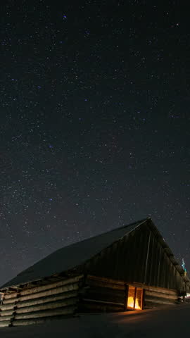 Time lapse of Star trails in the night sky, Wooden house in the mountains in winter, Stars move around a polar star, vertical footage