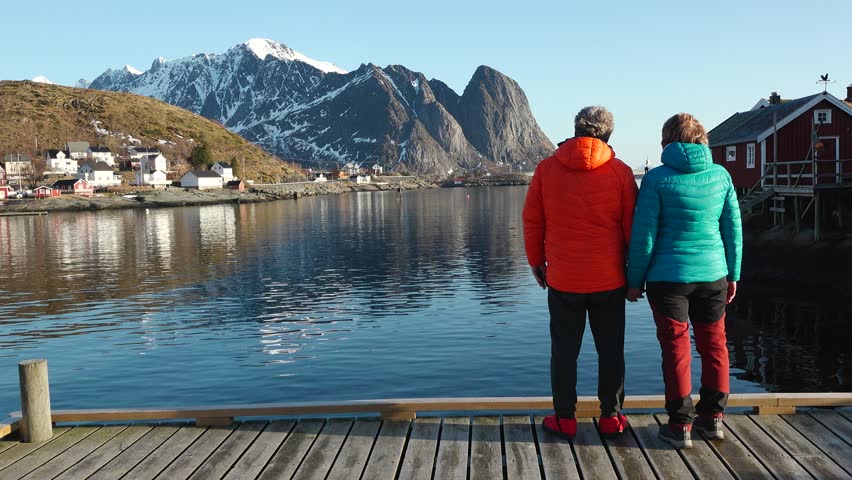 Travelers, walking on a beach surrounded by mountains. A happy loving mature couple enjoys a walk on the seashore in Norway. A man and a woman enjoy a beautiful nature of the Lofoten islands.