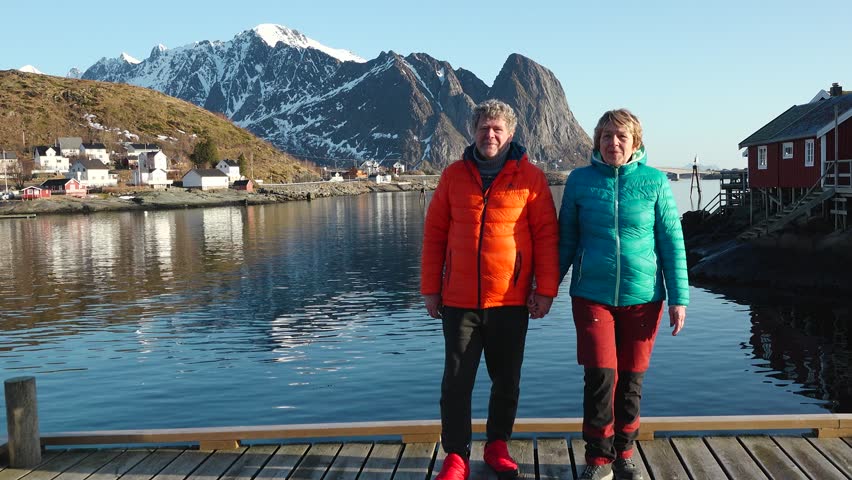 Travelers, walking on a beach surrounded by mountains. A happy loving mature couple enjoys a walk on the seashore in Norway. A man and a woman enjoy a beautiful nature of the Lofoten islands.