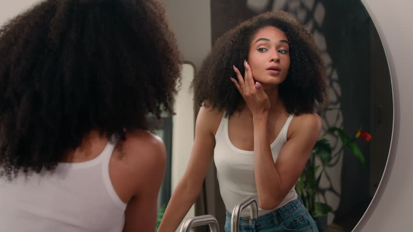 Morning beauty routine procedure healthy happy smiling pretty beautiful African American girl woman female at home walk come in bathroom looking at mirror reflection check skin face touch go away