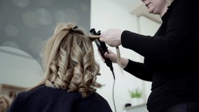 Hairdresser curls blonde hair with curling iron