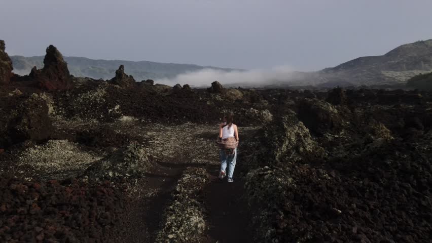 A girl traveler with a backpack walks through the mountains, against the backdrop of Mount Batur volcano, Bali island.