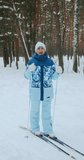 Vertical video, the camera zooms in on a happy woman of retirement age, who smiles and looks into the camera. A woman on classic skis in a winter forest. High quality 4k footage