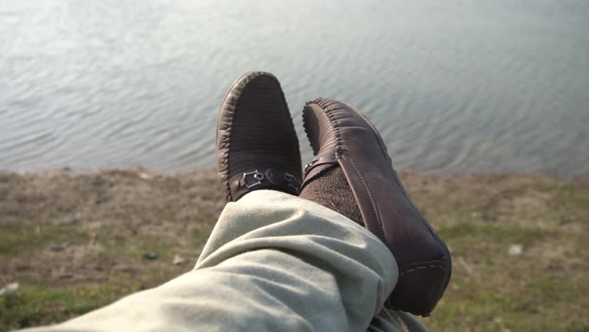 Feet of a man lying on the beach in 4k resolution. Young man lying in a camp tent closed up point of view on male legs with sea view on stunning beach at sunset.