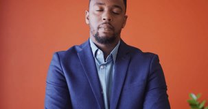 Video of smiling african american man looking at camera on orange background. business professionals and working in office concept.