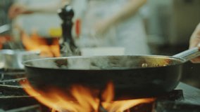 Close-up view of hands of master chef flipping food in frying pan as cooking on gas stove with burning fire flames in restaurant kitchen - Powered by Shutterstock - Get 15% off with code: PIKWIZARD15