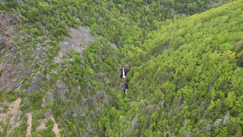 Drone shot going towards a small waterfall surrounded by trees located just off the famous Cabot Trail on Cape Breton Island in Nova Scotia, Canada shot during a beautiful summer day in 4k.