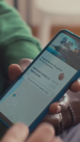 Close-up vertical shot of hands of unrecognizable young polyethnic couple choosing hotel for summer vacation abroad on booking website using smartphone app, zooming and scrolling to check its location