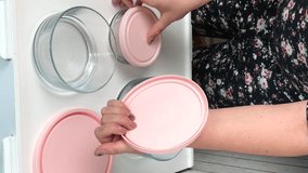A woman examines glass food containers with plastic lids. Reviews the purchase. Adds them one by one. Vertical video.