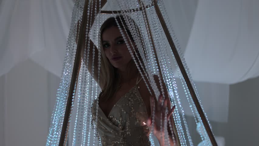 Caucasian beautiful and happy blonde woman in a shiny dress, standing on a golden sparkling chandelier, evening