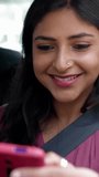 Happy young indian woman using cell phone sitting in the back seat of a car. Technology and transport concept. Vertical HD video.