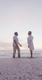 Vertical video of happy senior biracial couple proposing on sunny beach. healthy, active retirement beach holiday.