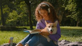 Caucasian woman young gen z student female domestic pet owner reading book on grass in city park outdoors smiling carefree girl in headphones rest on nature summer weekend with dog welsh corgi puppy - Powered by Shutterstock - Get 15% off with code: PIKWIZARD15