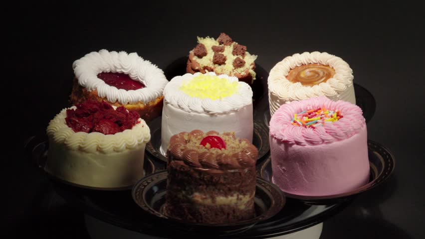 funny delicust mini personal mini cakes in turn table black background Small cakes petit turn table dessert table spinning cheesecake chocolate moka strawberry cheese butter