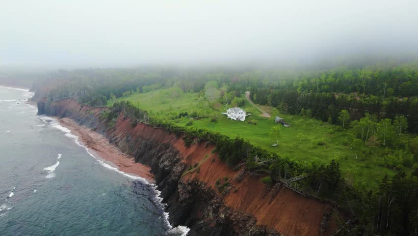 Drone shot on a really rainy and moody day of an isolated house build on a beautiful cliffs edge that meets the Atlantic Ocean located on Cape Breton Island, Nova Scotia in Canada shot in 4k.