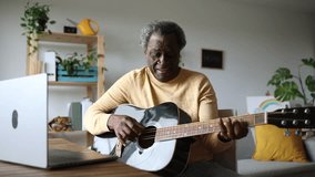 Senior African American man learning to play guitar at home with his online courses on his laptop