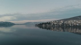Smooth drone shot of an Epic view, snow mountains, town on the lake, flying birds, dusk golden hour, European landscape, colorful houses reflection on the water, 4K video